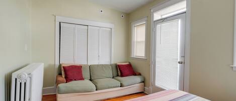 A bedroom with a bed, a radiator, a sofa, and a window with blinds.