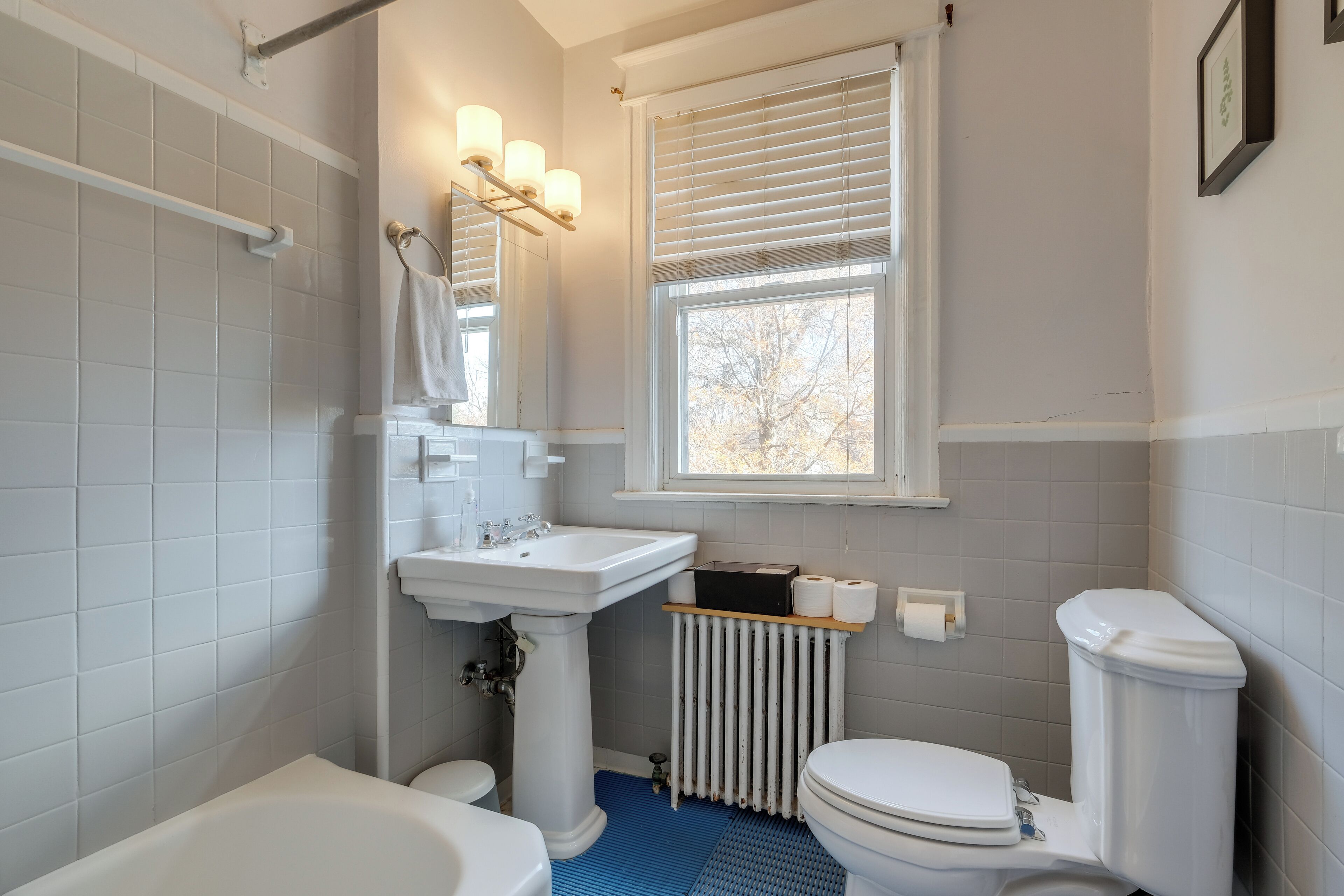 A bathroom with a bathtub, toilet, sink, and window with blinds.