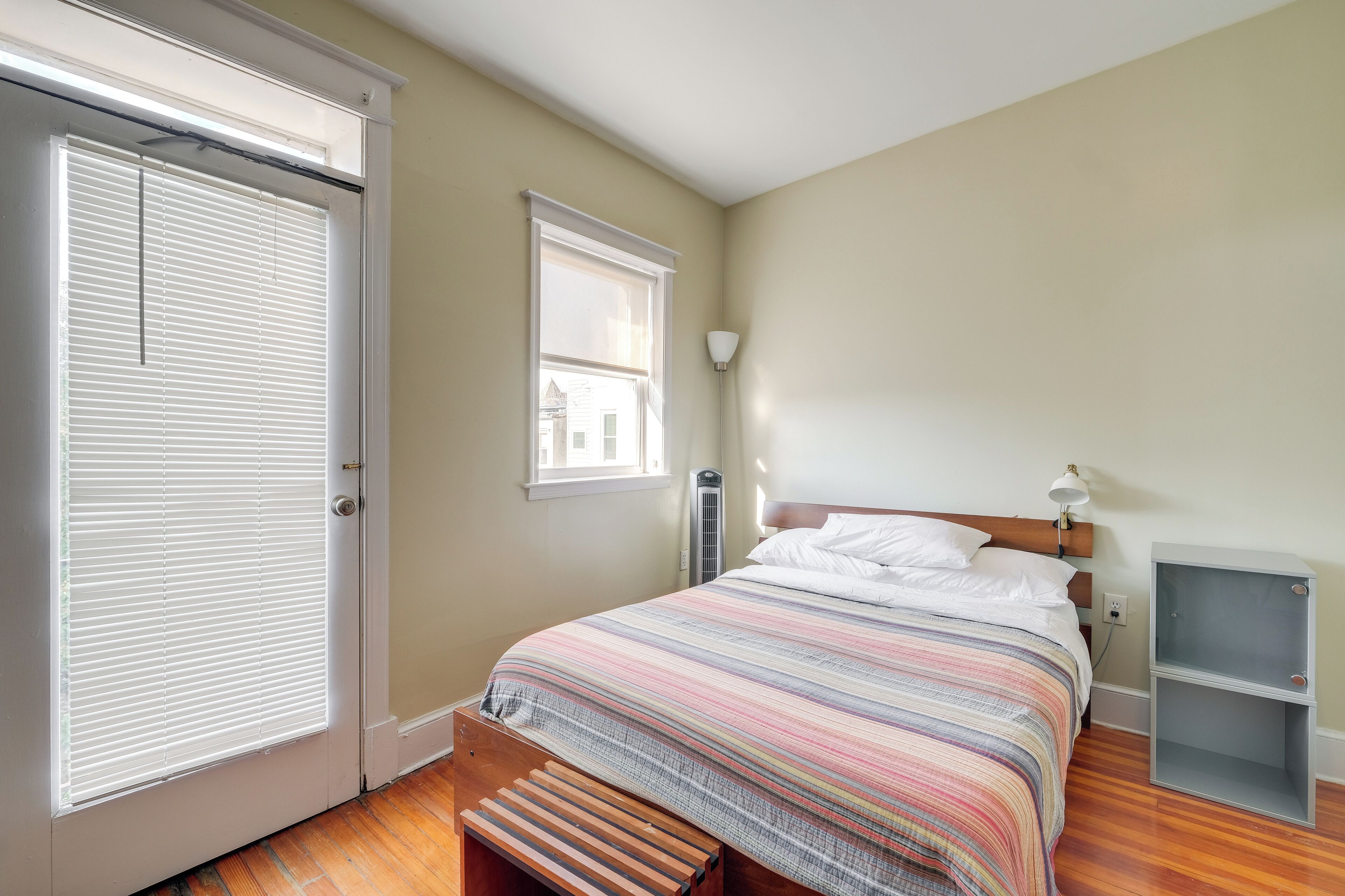 A bedroom with a bed, a bench, a nightstand, and a window with blinds.