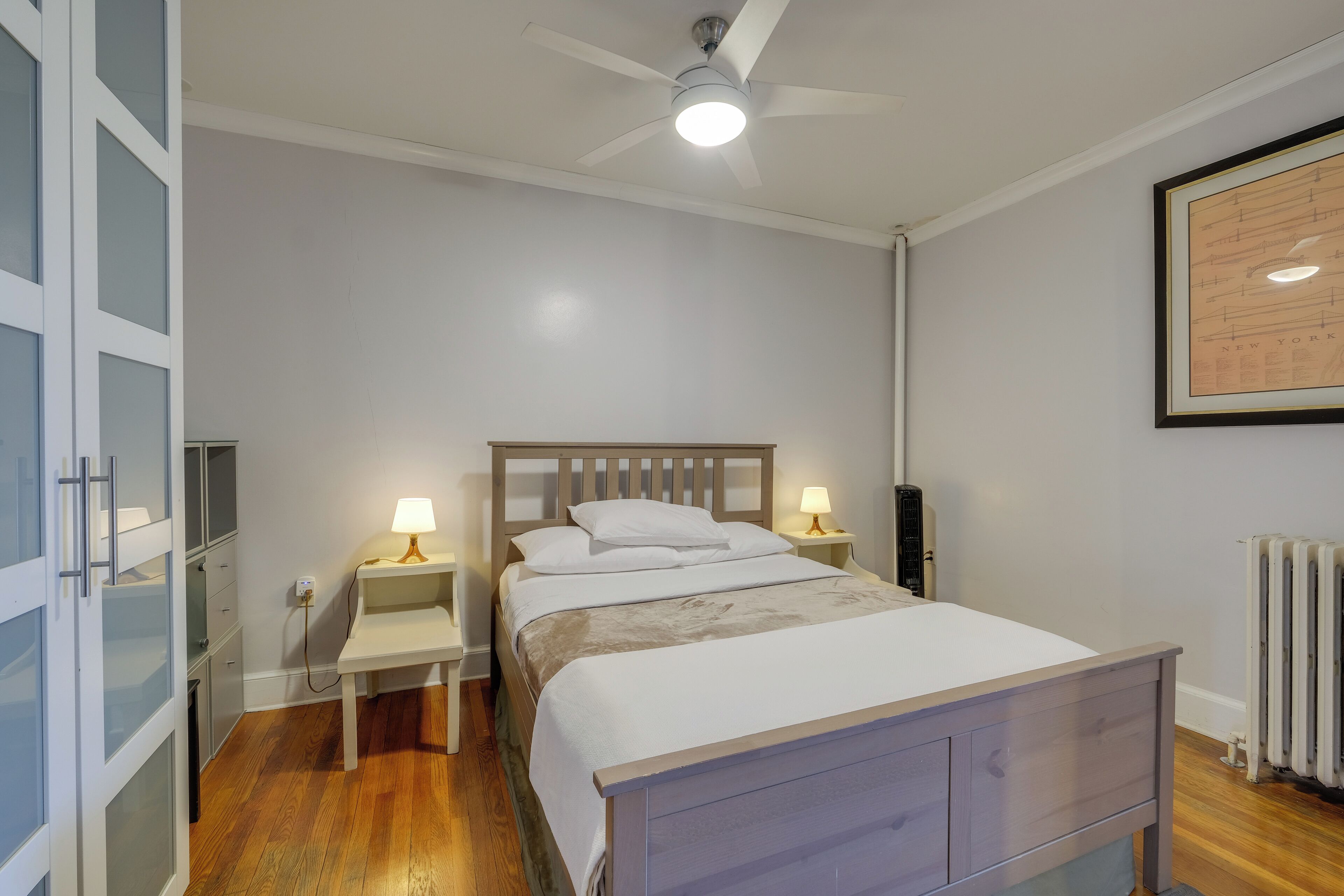 A bedroom with a bed, bedside lamps, a ceiling fan, and a radiator.