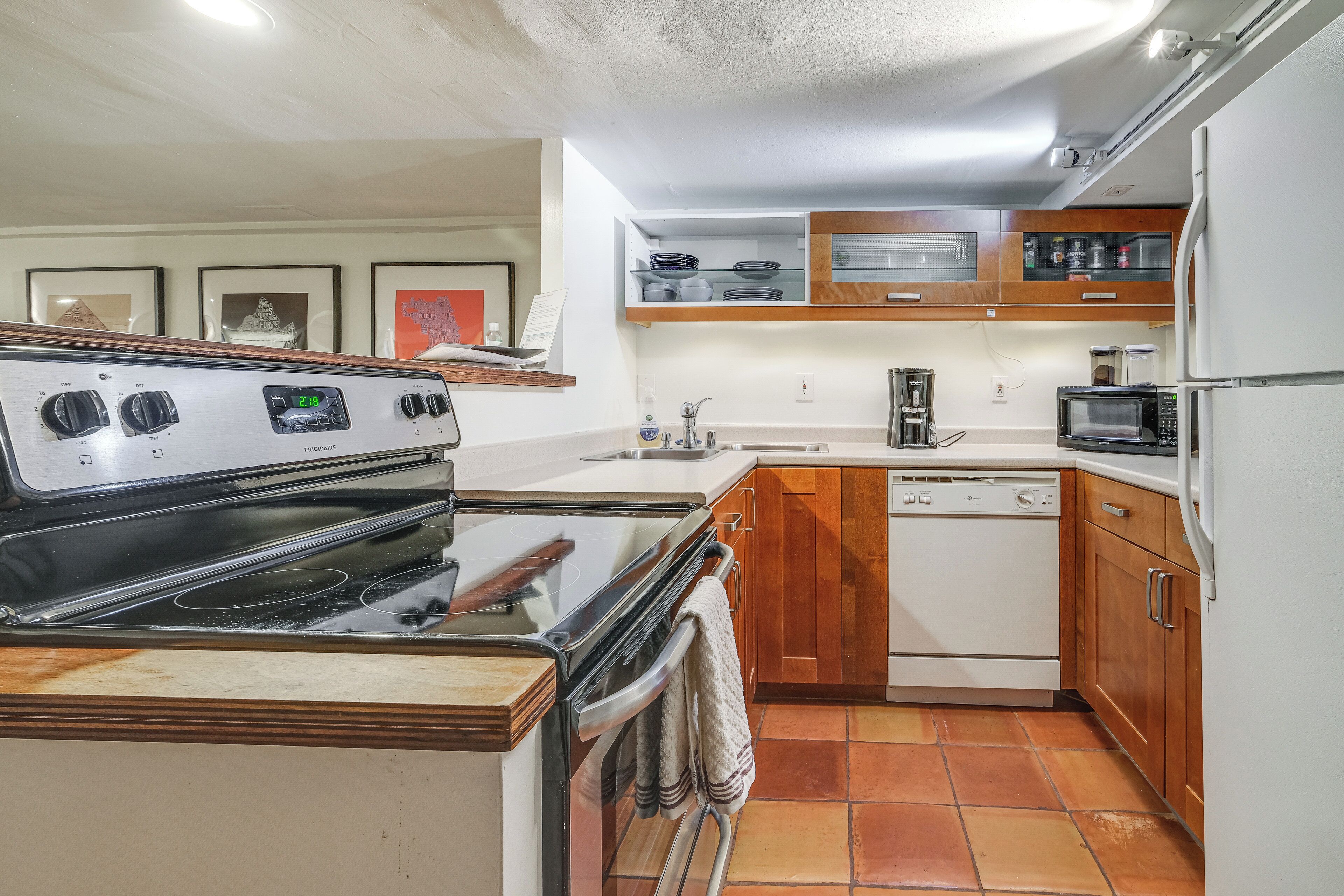 Cocina compacta con estufa, horno, microondas y lavavajillas. Cuenta con alacenas de madera y salpicadero de azulejos.