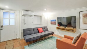 Ein Wohnzimmer mit grauem Sofa, einem orangefarbenen Sessel, einem Fernseher und einem gerahmten Bild an der Wand.