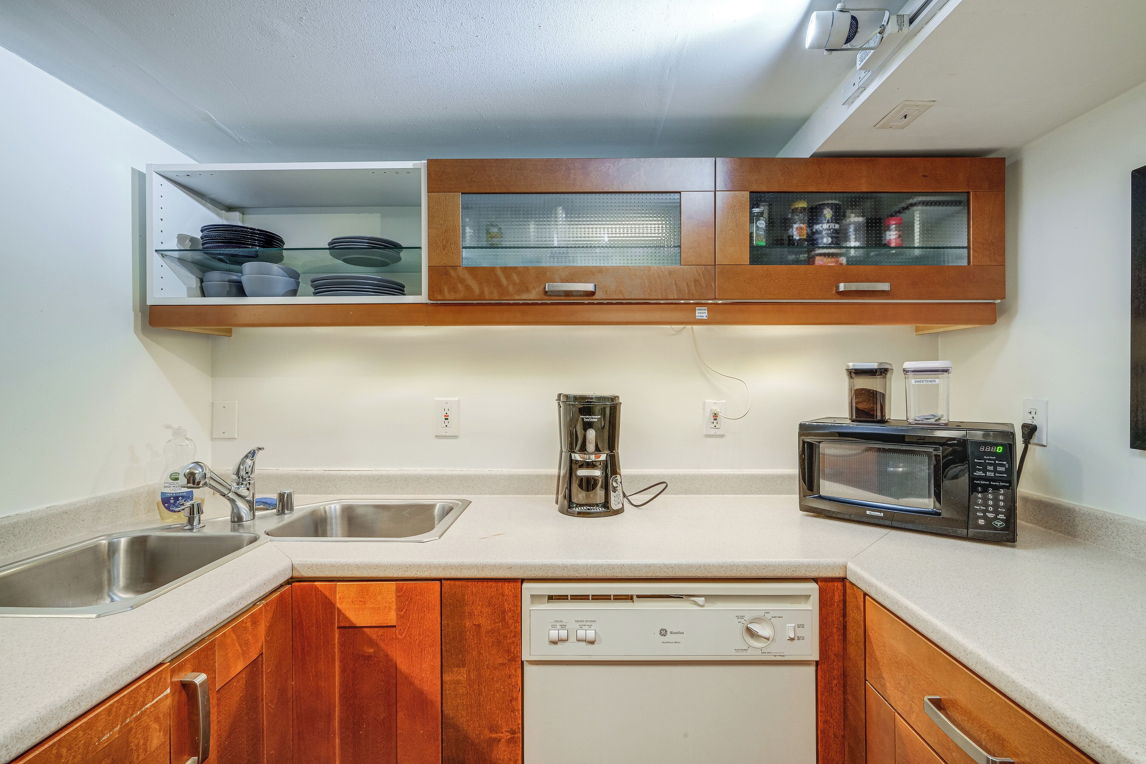 Una cocina con armarios de madera, lavavajillas, cafetera y microondas.
