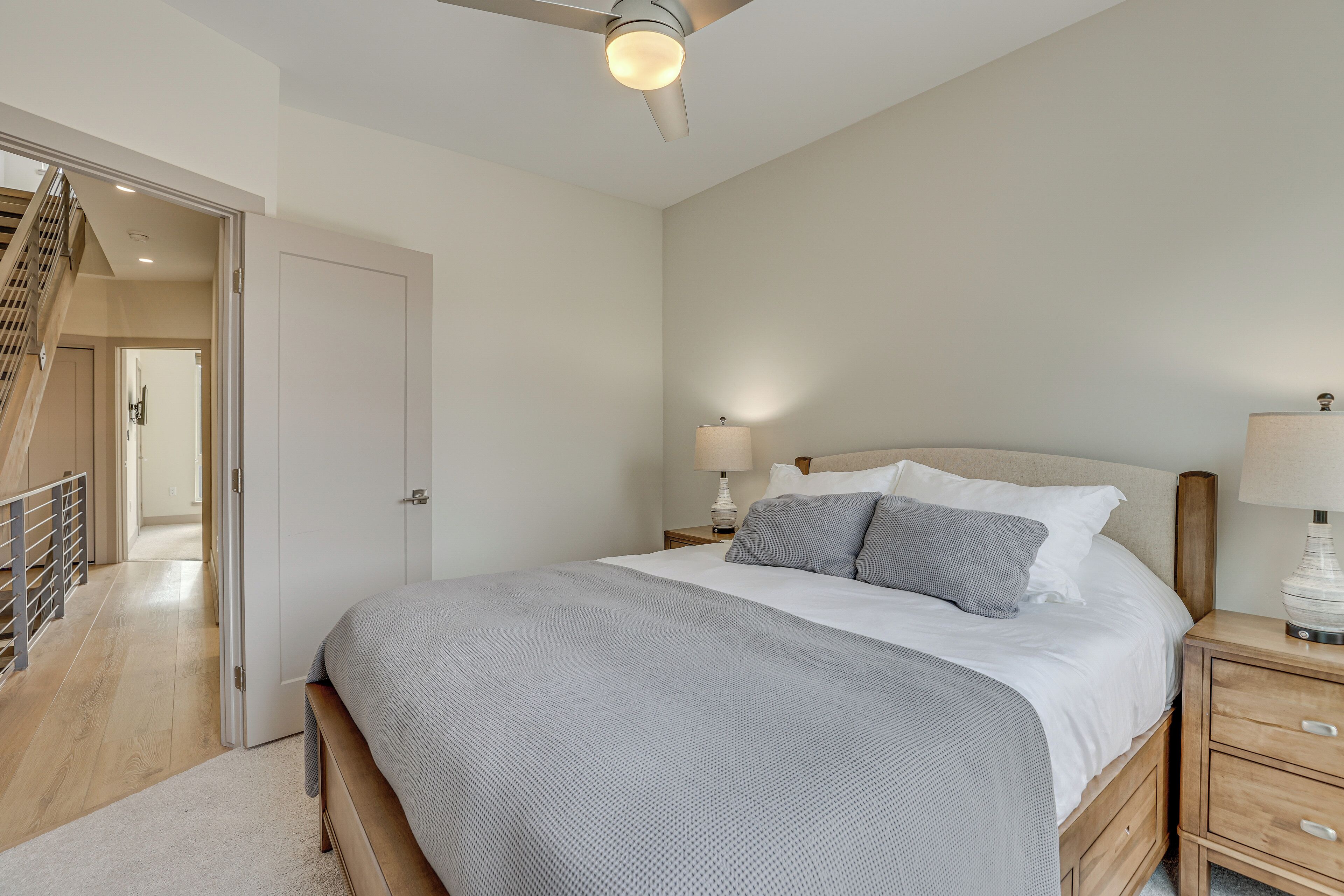 A bedroom with a bed, bedside tables, a lamp, a ceiling fan, and a staircase leading to another room.