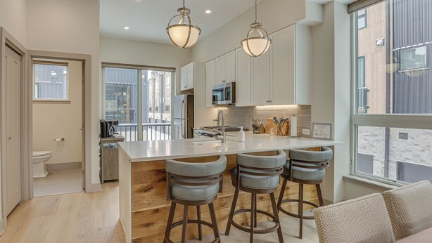 A modern kitchen with a central island, bar stools, and a large window providing a view of the city. - Silverthorne Townhome w/ Hot Tub: Walk to Town! (Silverthorne)