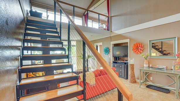 A multi-level interior with a wooden staircase, a red sofa, a television, and a decorative flower. - Kailua-kona Condo Rental ~ 1/2 Mi to Golf Course! (Kailua-Kona)