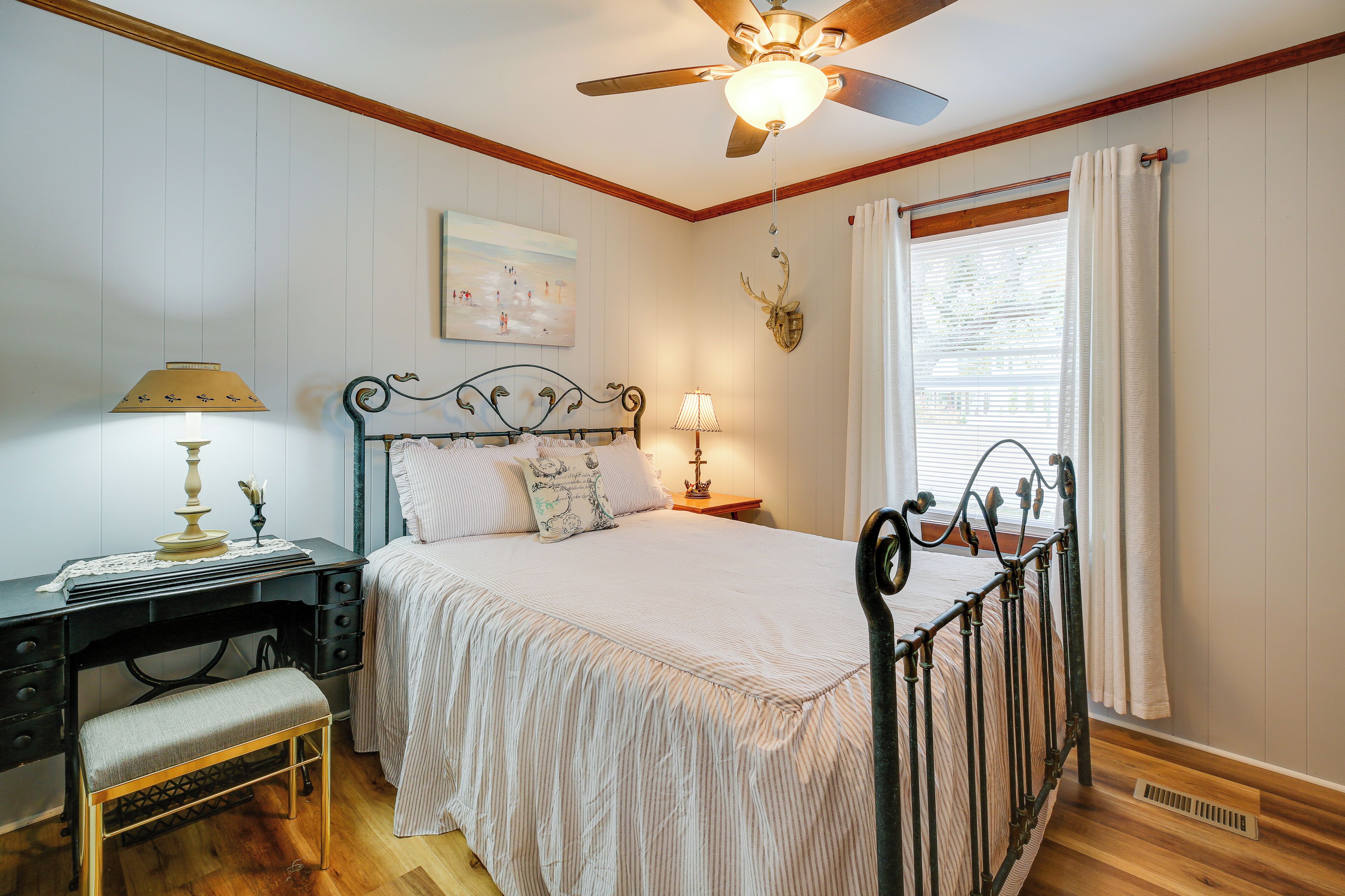 Une chambre à coucher comprenant un lit, des tables de chevet, un bureau, une chaise, un ventilateur de plafond et une fenêtre avec des rideaux.