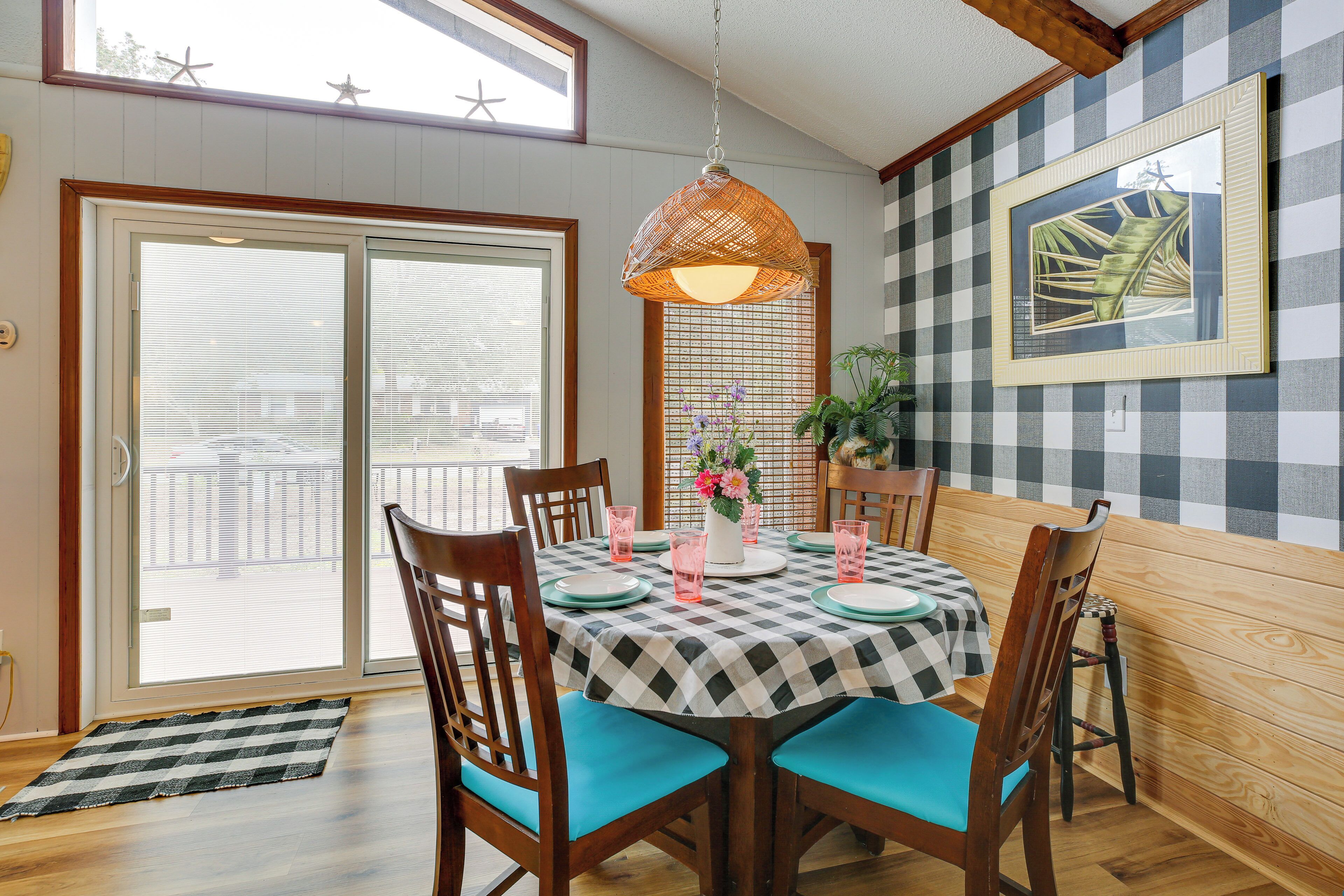 A dining area with a checkered tablecloth, wooden chairs, and a hanging light fixture.