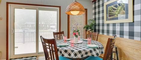 A dining area with a checkered tablecloth, wooden chairs, and a hanging light fixture.