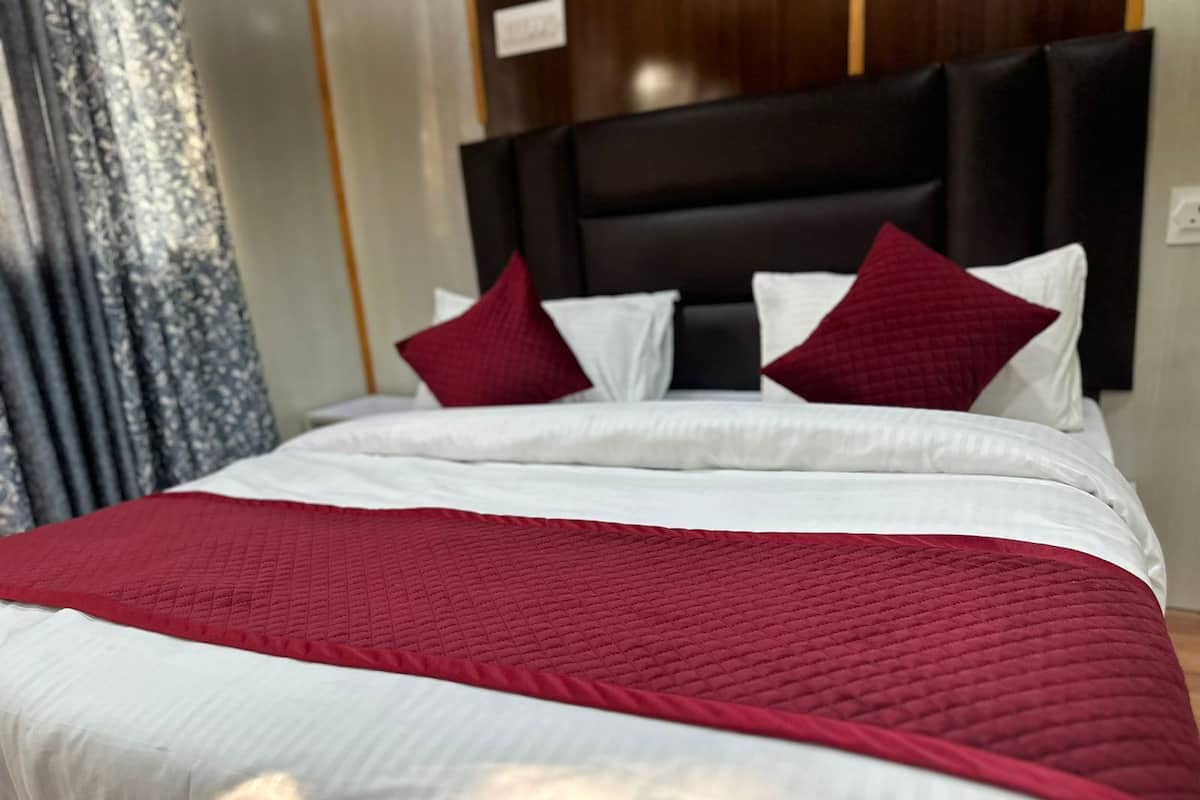 A neatly made bed with white and red bedding, a dark headboard, and a curtain in the background.