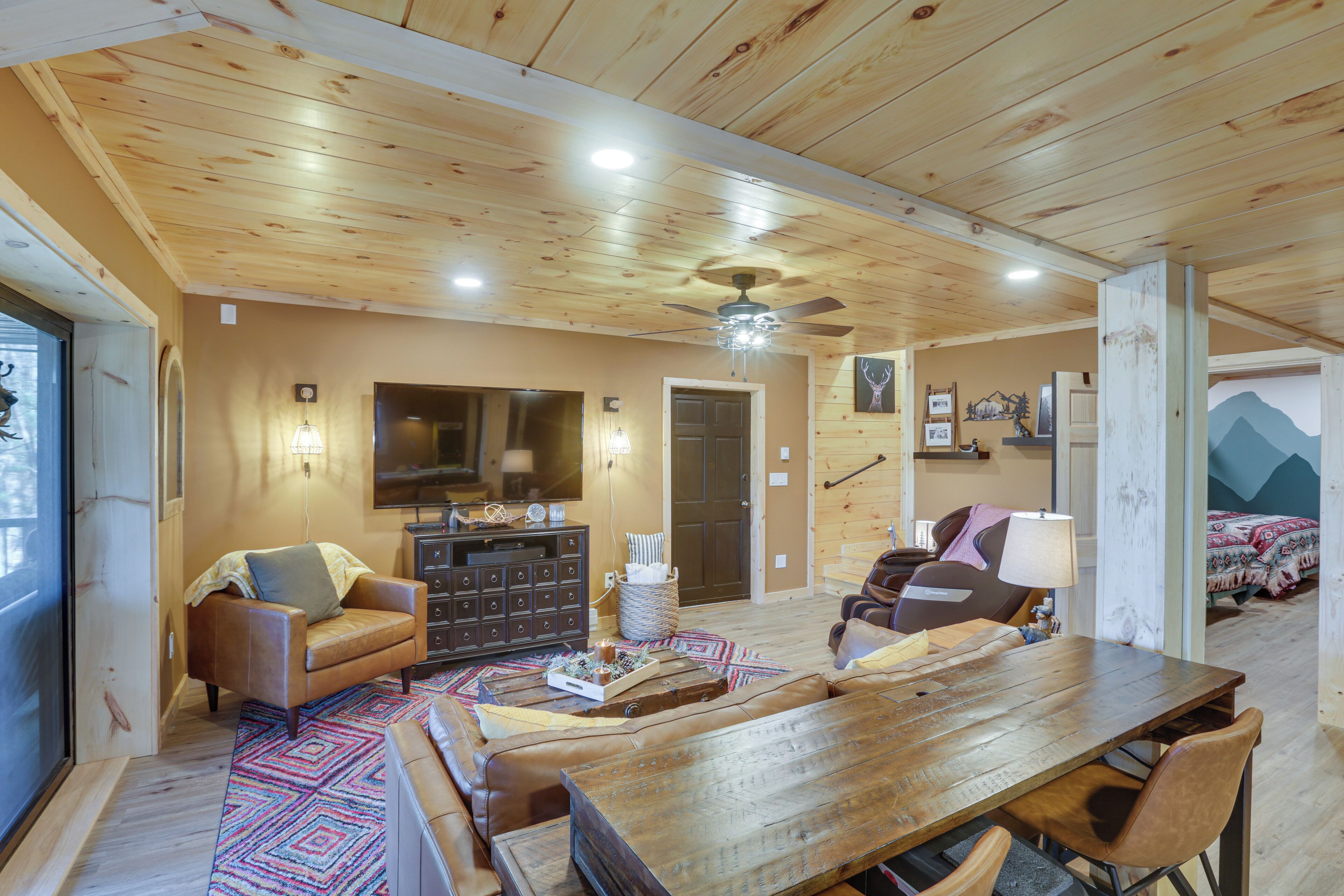 A cozy cabin interior with a wooden ceiling, a dining table, a sofa, and a fireplace.
