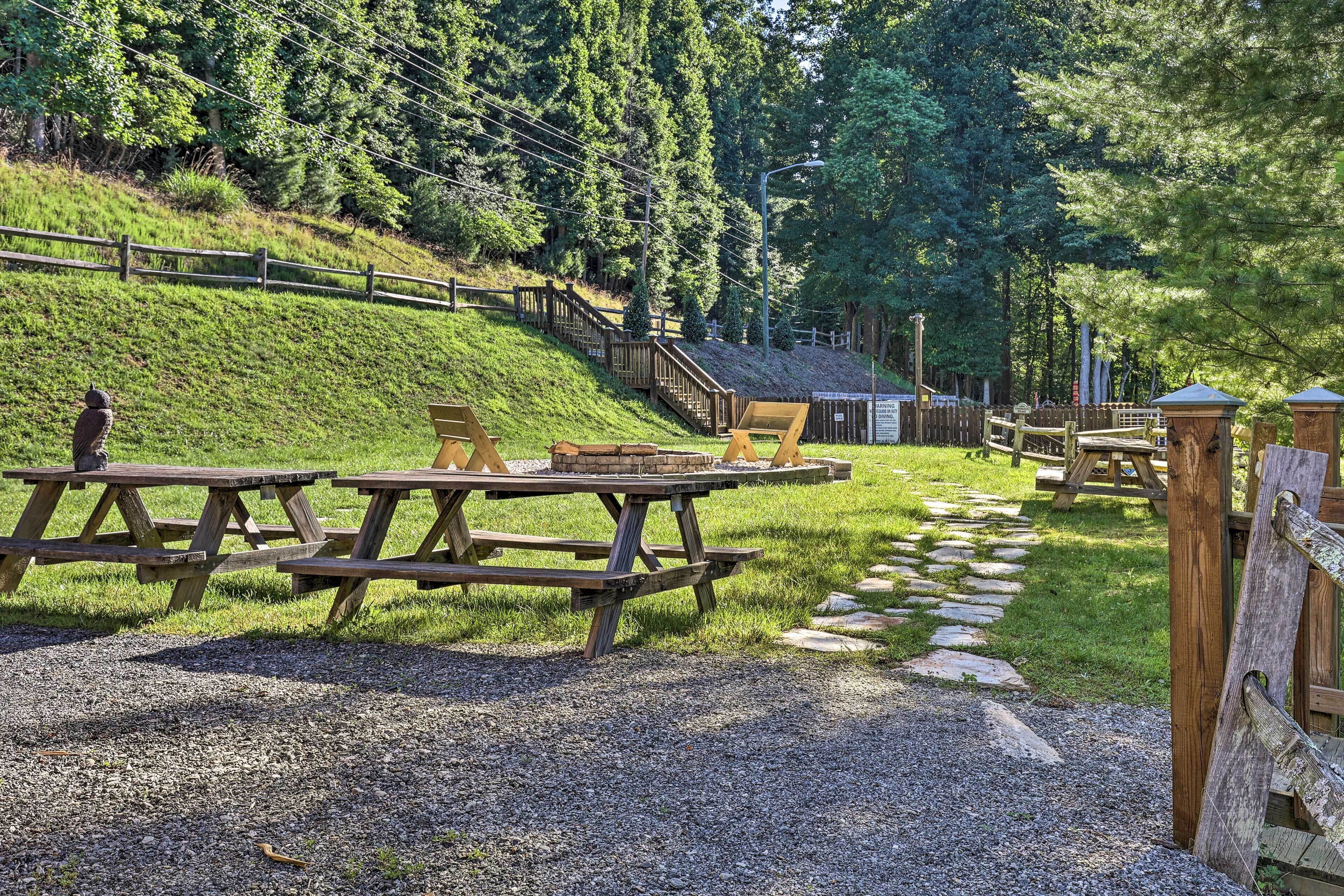 A picnic area with wooden benches and picnic tables, surrounded by a wooden fence and a stone path.