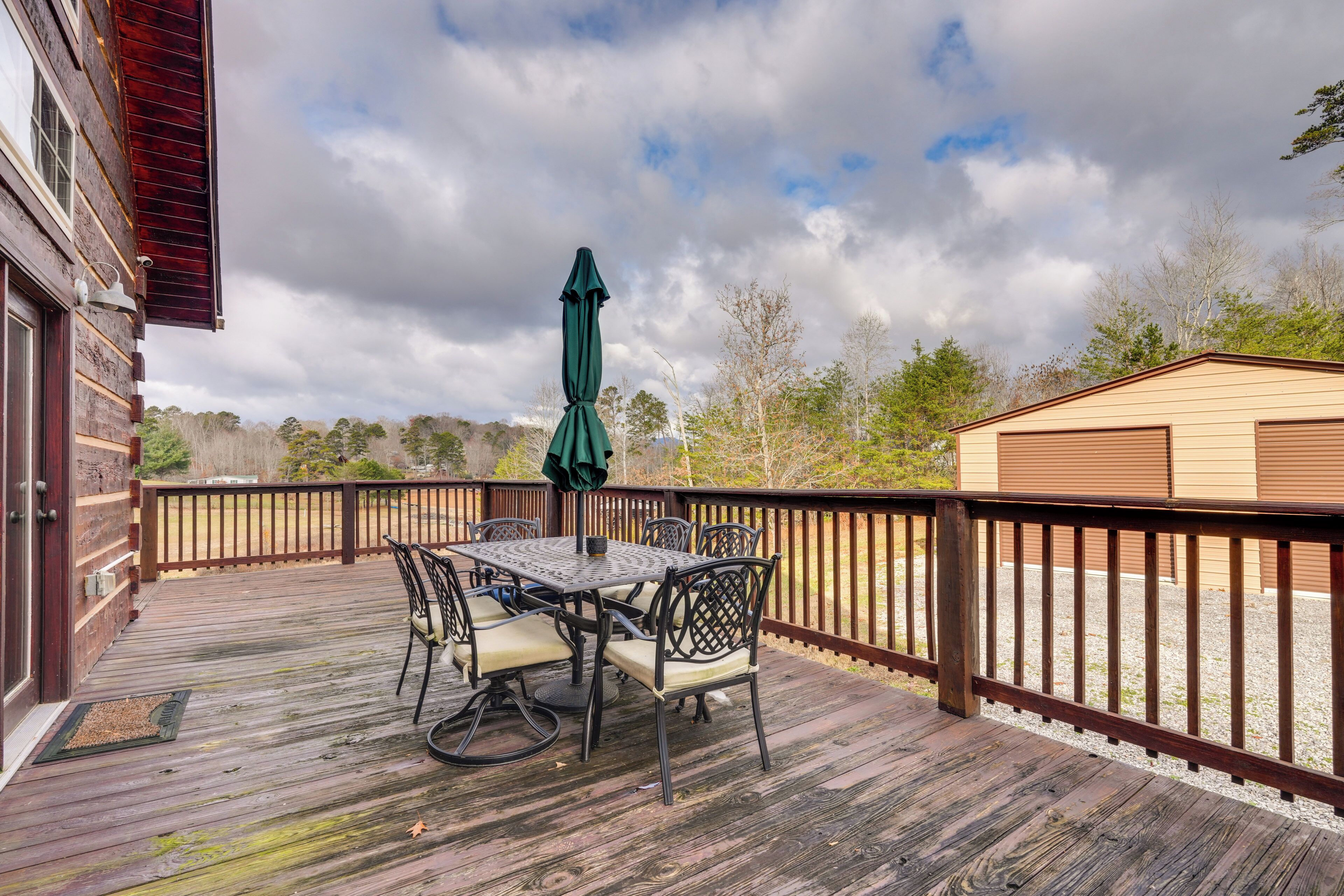 A wooden deck with a table and chairs, a green umbrella, and a wooden fence.