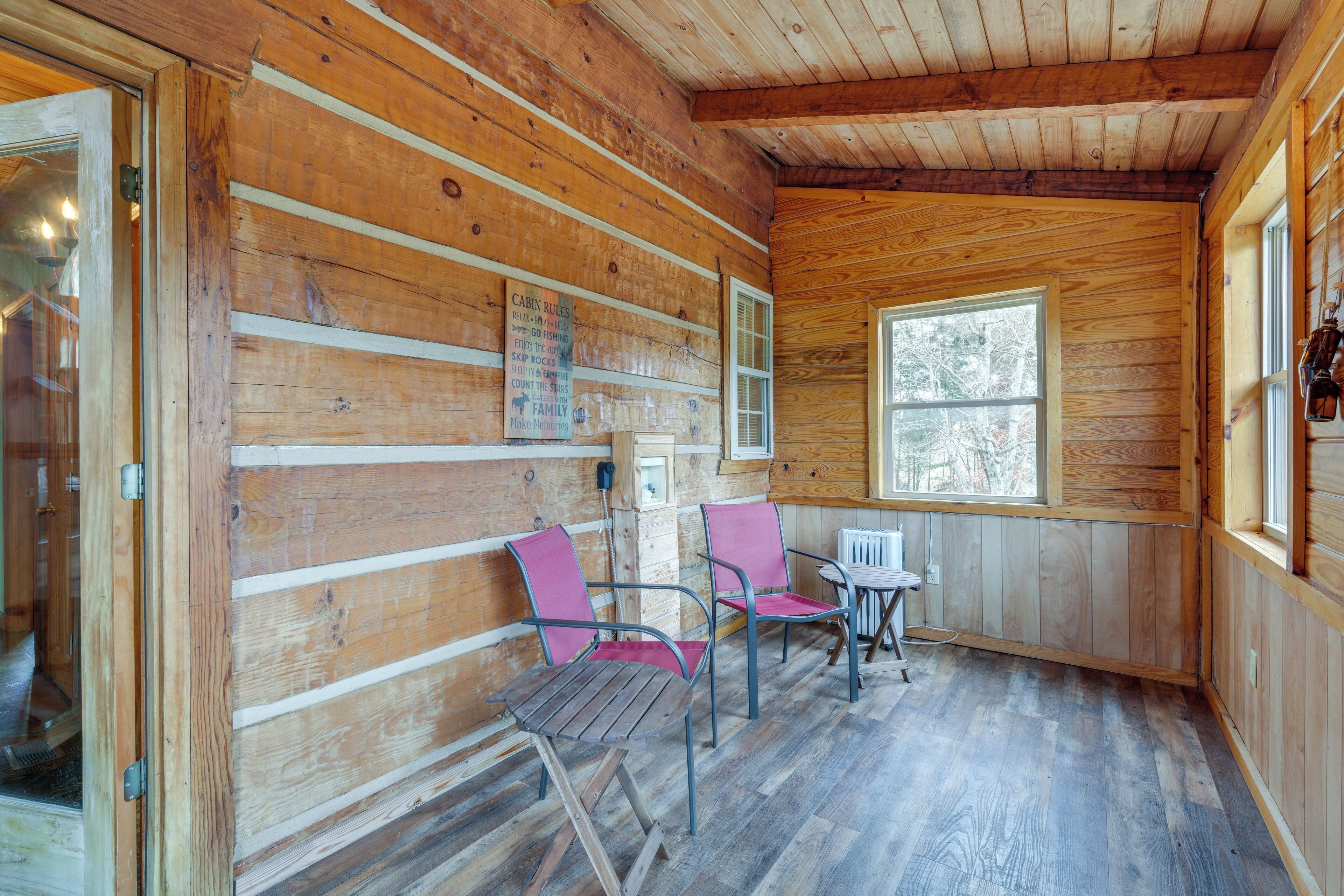A cabin interior with wooden walls, a window, a table, and two chairs.