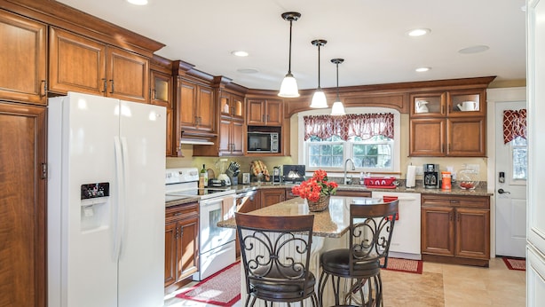 A kitchen with wooden cabinets, a white refrigerator, a microwave, and a large island with bar stools.