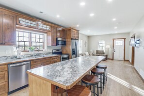 Una cocina moderna con armarios de madera, encimera de granito, electrodomésticos de acero inoxidable y una zona de bar con taburetes.