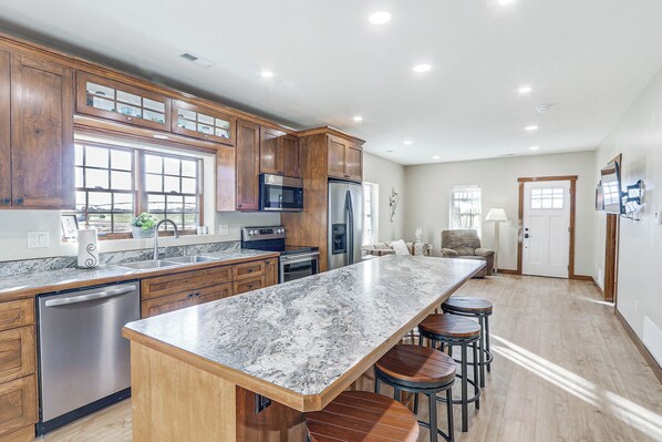 A modern kitchen with wooden cabinets, a granite countertop, stainless steel appliances, and a bar area with stools. - Secluded Sterling Vacation Rental - Pet Friendly! (Sterling)
