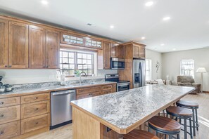 Una cocina con armarios de madera, encimera de granito, electrodomésticos de acero inoxidable y una zona con taburetes de bar.