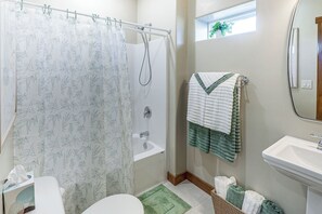 Un bany amb cortina de dutxa, banyera, un lavabo i una finestra amb una planta.
