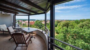 Un balcon avec une table et des chaises, offrant une vue panoramique sur une ville côtière et la verdure environnante.