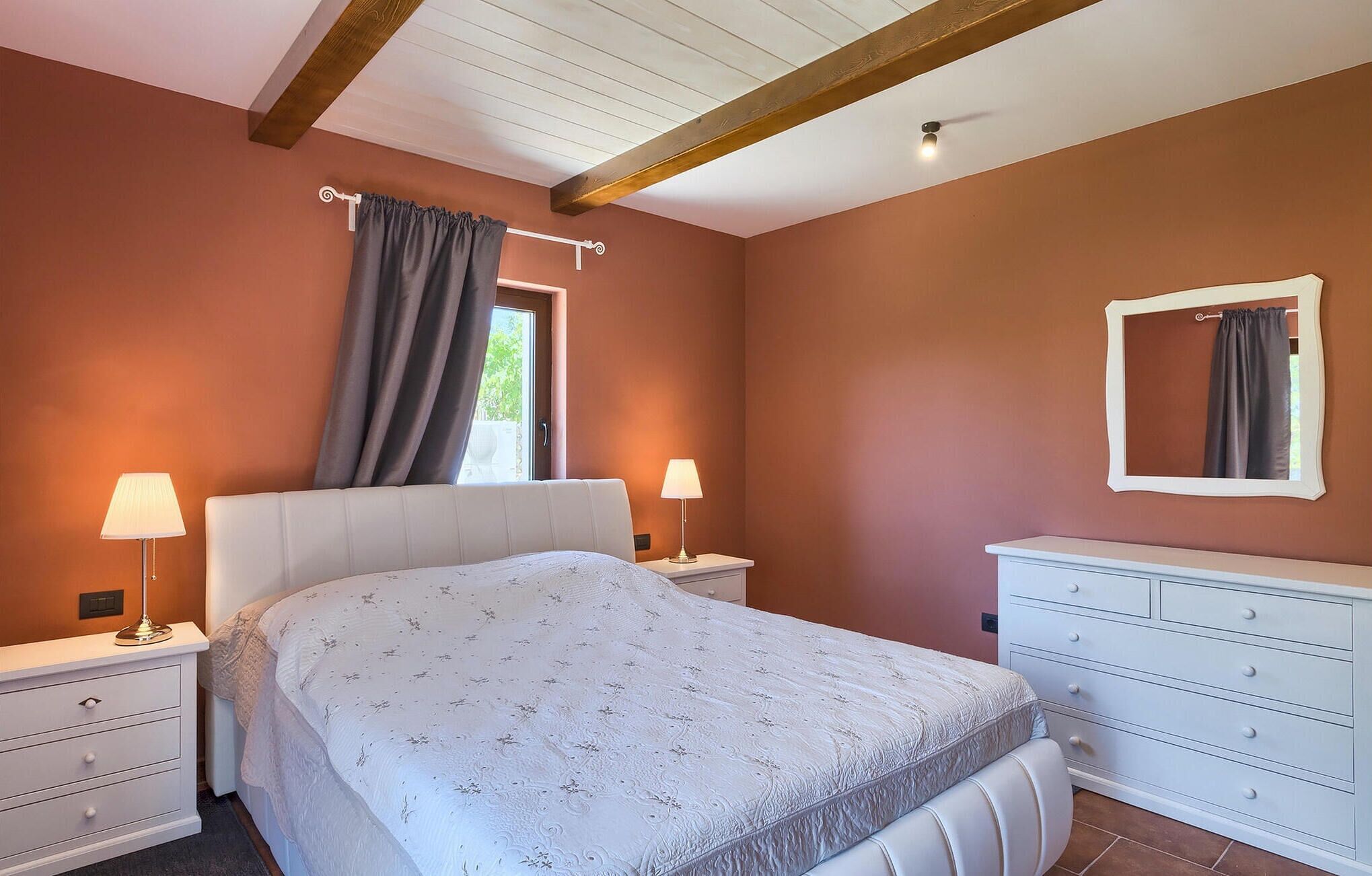 A bedroom with a bed, bedside tables, a dresser, and a window with curtains.