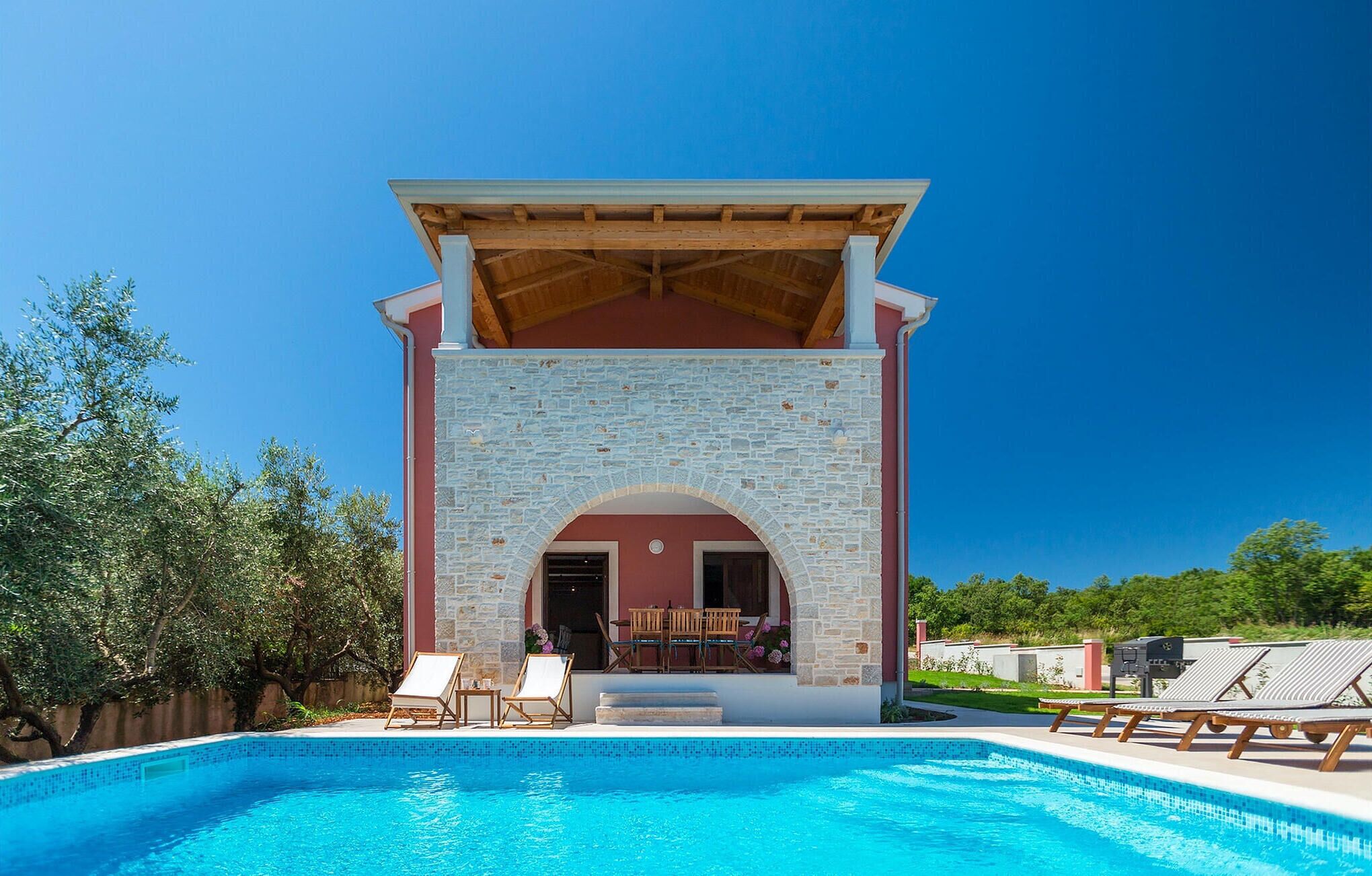 Une piscine agrémentée d’une arche en pierre et d’un patio couvert.