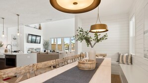 Ett modernt matområde med en träbänk, ett bord i mitten med en vävd bordsduk och en hängande lampa.