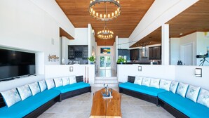 A spacious living area with a large wooden coffee table, two blue sofas with matching cushions, and a modern chandelier. - Sky Beach Club Villa Waterfall 2 4 Bedroom Home (Governor's Harbour)