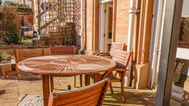 Une terrasse extérieure avec une table ronde en bois et quatre chaises en bois.