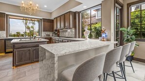 A modern kitchen with a large island, dark wood cabinets, and a chandelier. - Tudor Revival Castle with Bay Views 5bd / 5 bath (Mill Valley)