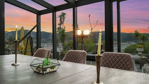 A dining table with candles, a glass terrarium, and a view of a sunset over mountains. - Tudor Revival Castle with Bay Views 5bd / 5 bath (Mill Valley)