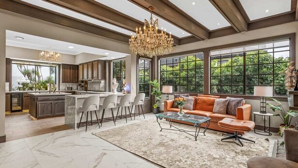 A spacious living area with a large window, a chandelier, and a modern kitchen in the background. - Tudor Revival Castle with Bay Views 5bd / 5 bath (Mill Valley)