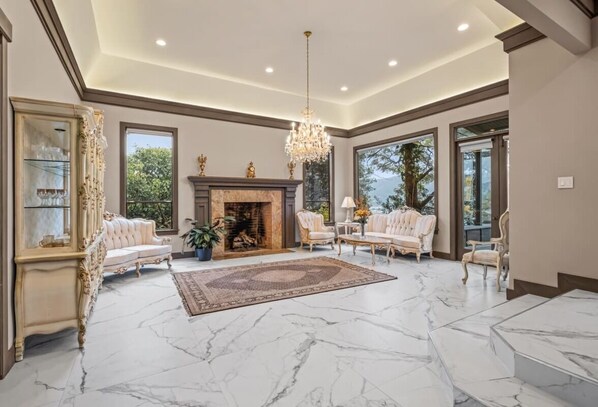 A spacious living room with a marble floor, a fireplace, and elegant furniture.