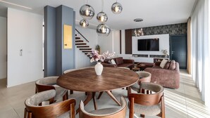 A modern living room with a round wooden dining table, leather sofas, and a TV mounted on the wall. - Villa Barbara Pakostane (Pakostane)