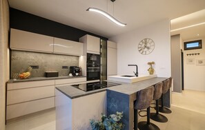 A modern kitchen with a central island, a built-in oven, and a wall-mounted clock. - Villa Barbara Pakostane (Pakostane)