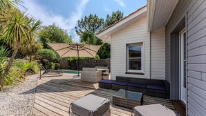 Une terrasse en bois avec des meubles d’extérieur, une piscine et une maison aux murs recouverts de bardage blanc.