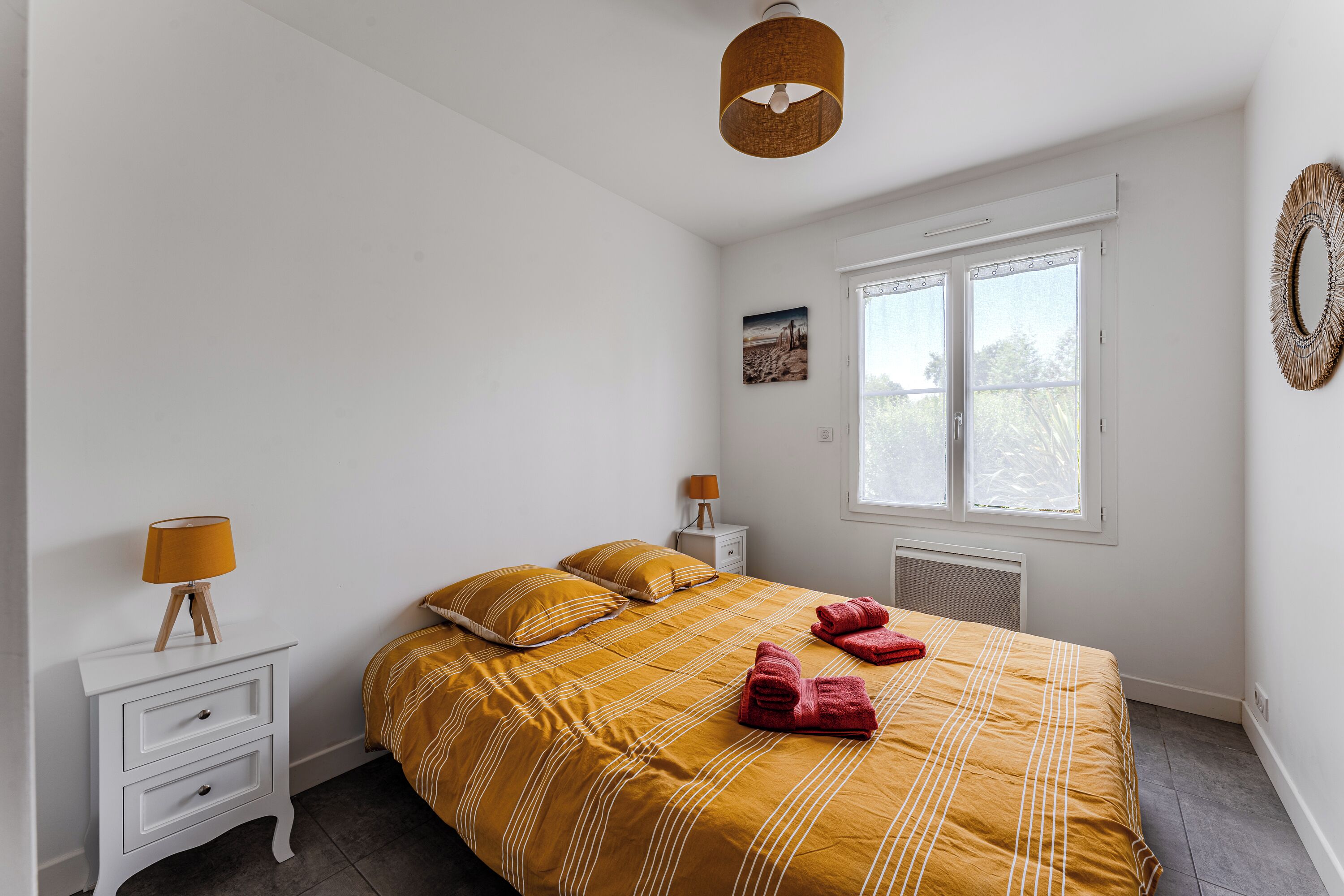 Een slaapkamer met een bed, witte nachtkastjes, een raam en een hanglamp.