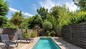 Une piscine rectangulaire dotée d’une terrasse en bois, entourée d’une clôture en bois et d’une végétation luxuriante.