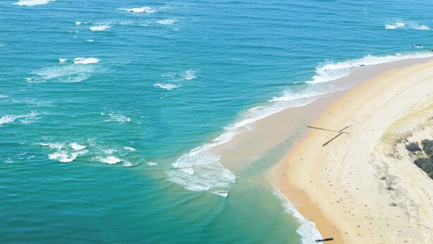 Une vue aérienne d’une plage aux eaux d’un bleu limpide et au rivage sablonneux.