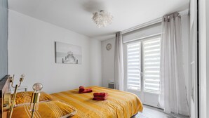 Une chambre à coucher avec un lit, une table de chevet, une lampe, une fenêtre avec des rideaux et une horloge murale.