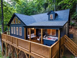 A cabin with a deck, a hot tub, and a covered seating area.