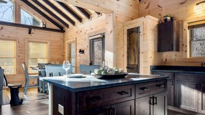 A wooden cabin interior with a kitchen area, dining table, and chairs. - Peaceful Mountain Escape with Ridge Views & Hot Tub (Maggie Valley)