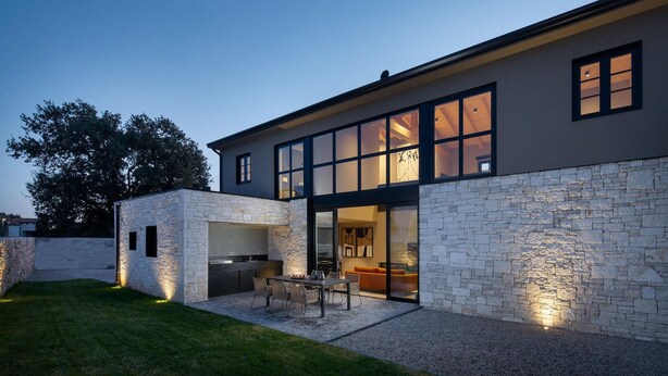 A modern house with a stone exterior, large windows, and an outdoor dining area.
