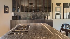 A modern kitchen with a central island, dark cabinetry, and a marble backsplash.