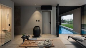 A modern spa room with a wooden sauna, a large black vase, a wooden bench, and a view of a swimming pool.