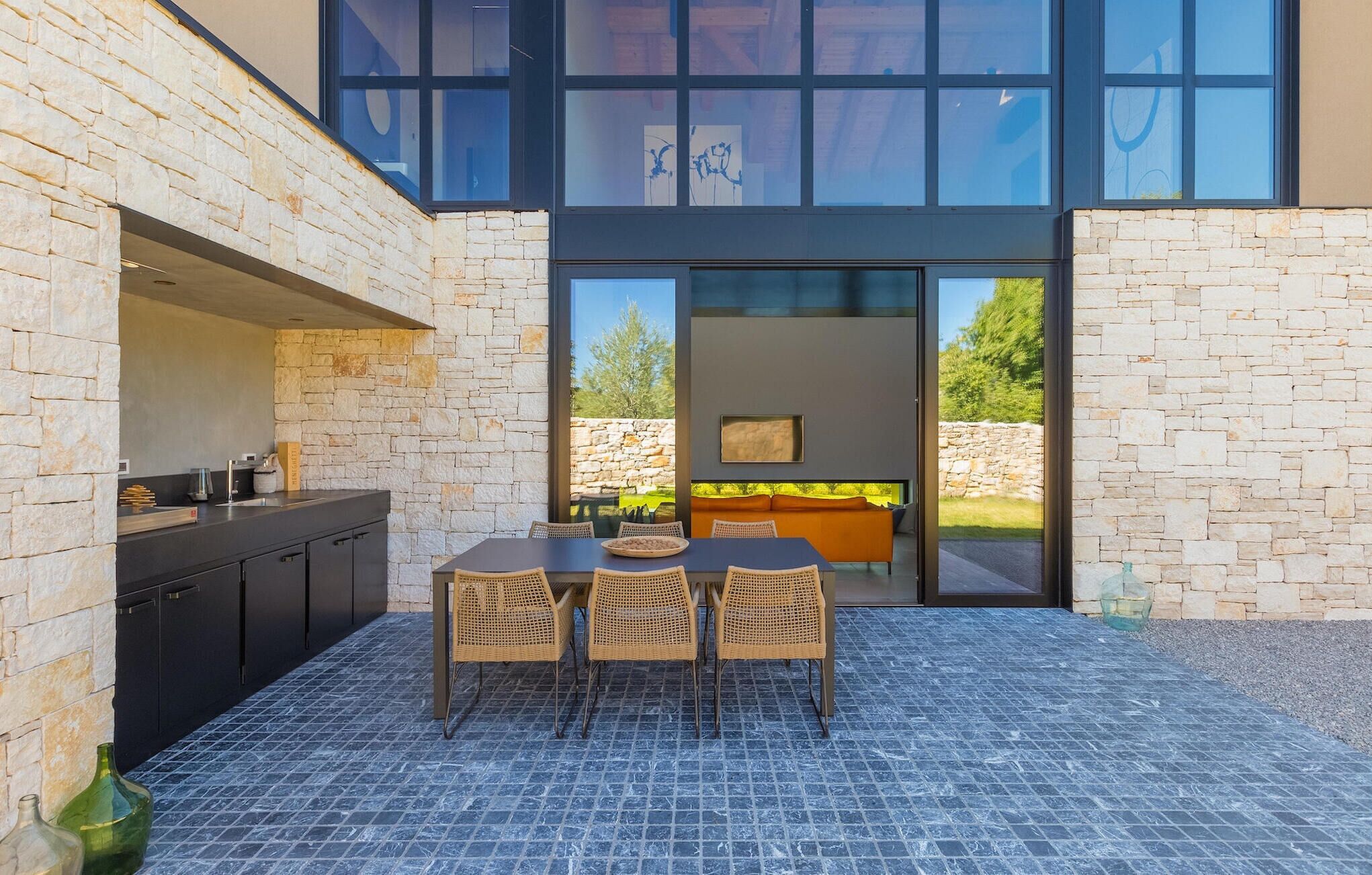 A modern outdoor dining area with a stone wall, a grill, and a view of the garden.
