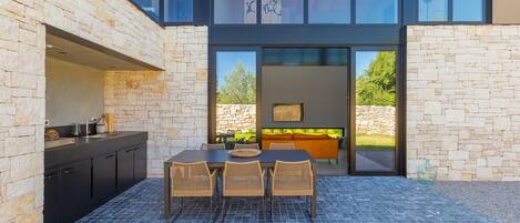A modern outdoor dining area with a stone wall, a grill, and a view of the garden.