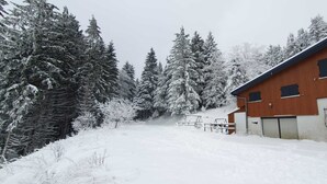Paisaje nevado con un edificio de madera, un área cercada y árboles cubiertos de nieve.