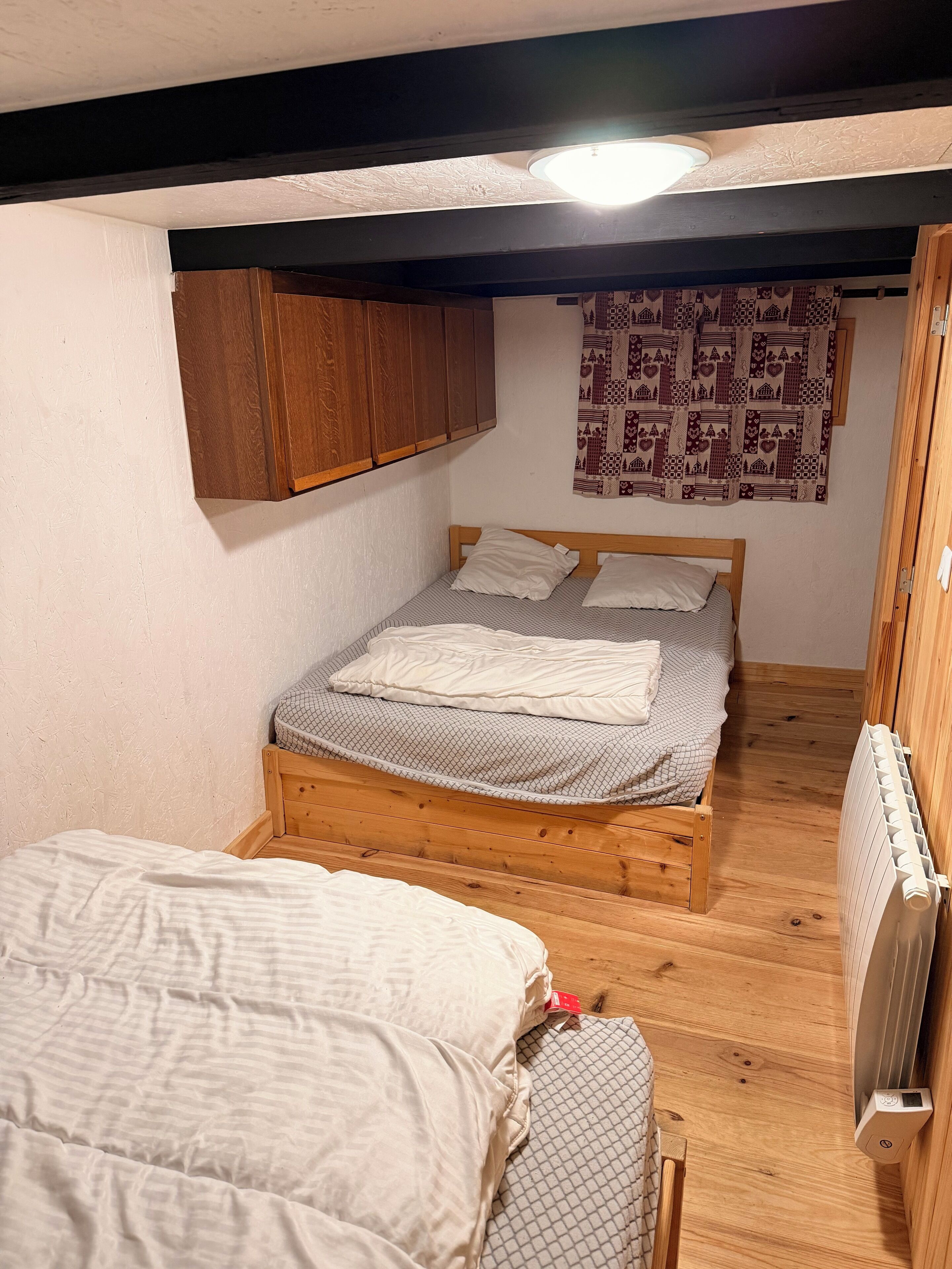 A small, cozy bedroom with a single bed, a wooden wardrobe, and a patterned curtain.