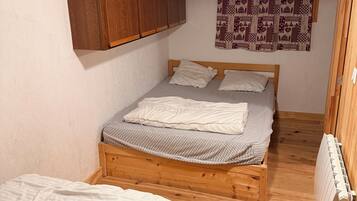 A small, cozy bedroom with a single bed, a wooden wardrobe, and a patterned curtain.